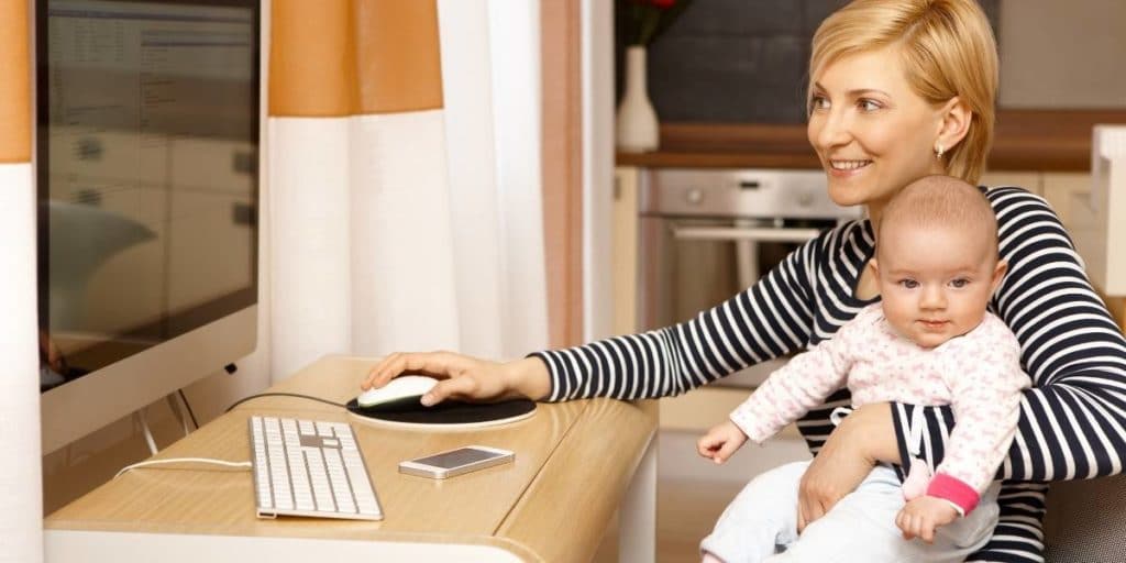 Mother holding baby and using a computer with one hand