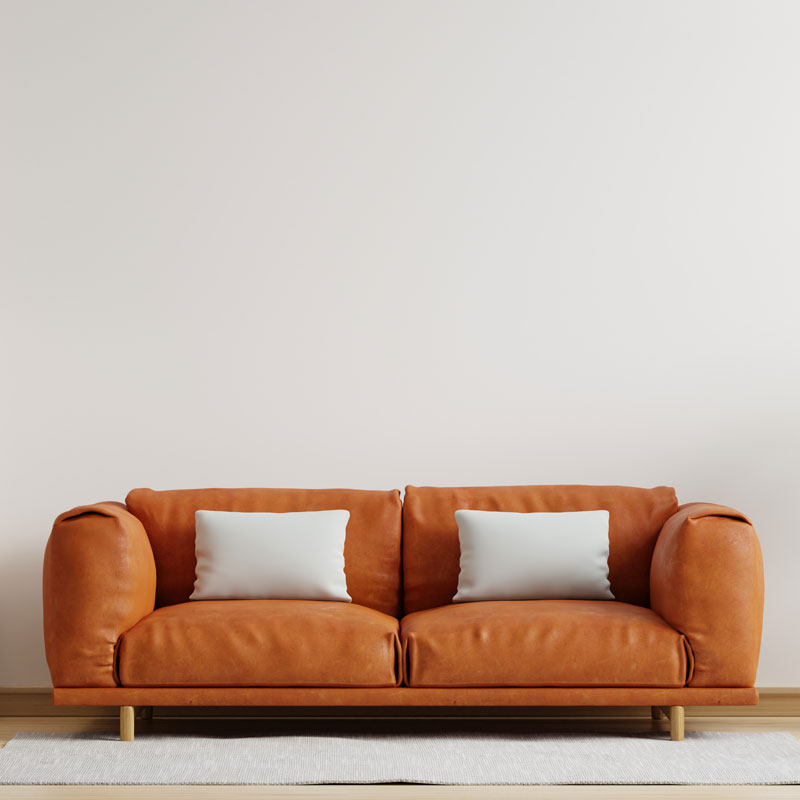 A modern, low-back, orange, leather couch against a white wall with two white pillows propped up on it